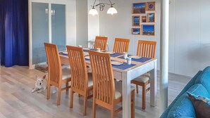 A dining area with a table set for six, surrounded by wooden chairs, and a small dog on the floor.