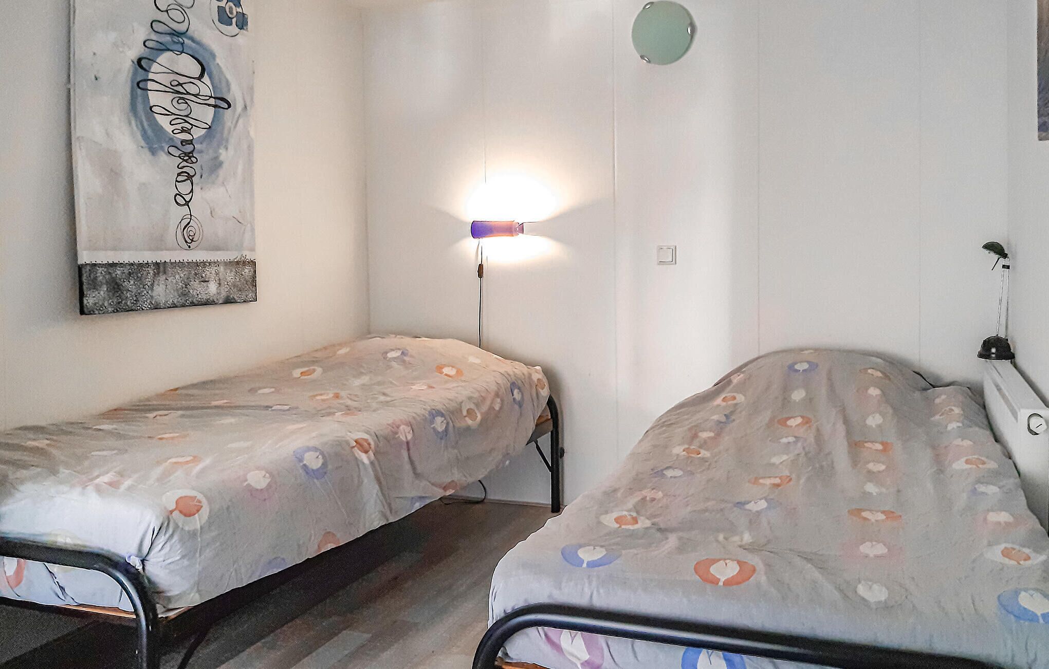 A room with two single beds, a wall-mounted lamp, and a painting.