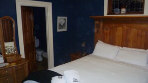 Un dormitorio con cabecera de madera, cama con ropa blanca, mesita de noche con lámpara y cómoda con espejo.