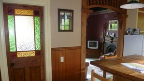 Una mesa de comedor de madera con sillas, una puerta de vitral, un televisor y una lavadora al fondo.