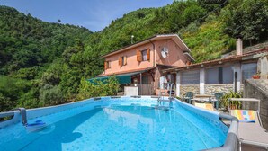 Una piscina con plataforma de baldosas, rodeada por una casa de fachada de piedra, con colinas verdes y exuberantes al fondo.