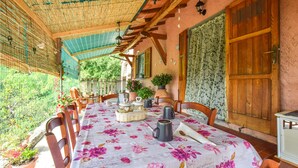 Un patio techado con una mesa dispuesta para comer, rodeado de sillas y una puerta de madera a la derecha.