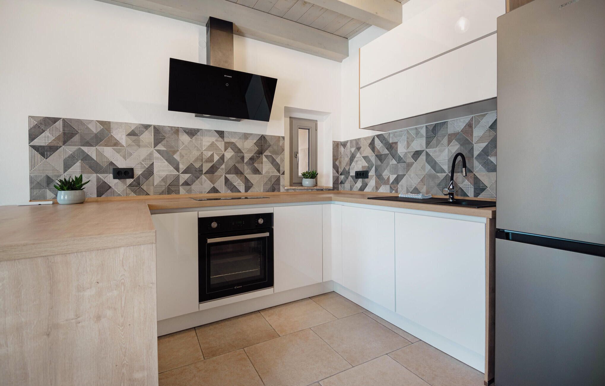 A modern kitchen with white cabinetry, a built-in oven, a stainless steel refrigerator, and a flat-screen TV mounted above the oven.