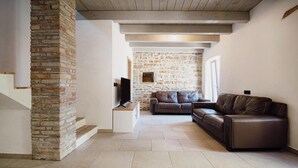 A spacious living area with a stone wall, a brown leather sofa, and a television on a stand.