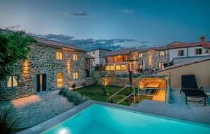 A stone villa with a swimming pool, outdoor seating, and a well-lit garden at dusk. - Awesome home in Skofije (Skofije)