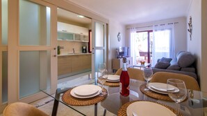 Un comedor con mesa de vidrio, individuales tejidos y una botella de vino tinto.