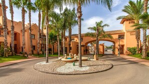 Un patio con palmeras, una fuente circular y un edificio con techo de tejas.