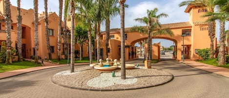 Un patio con palmeras, una fuente circular y un edificio con techo de tejas.