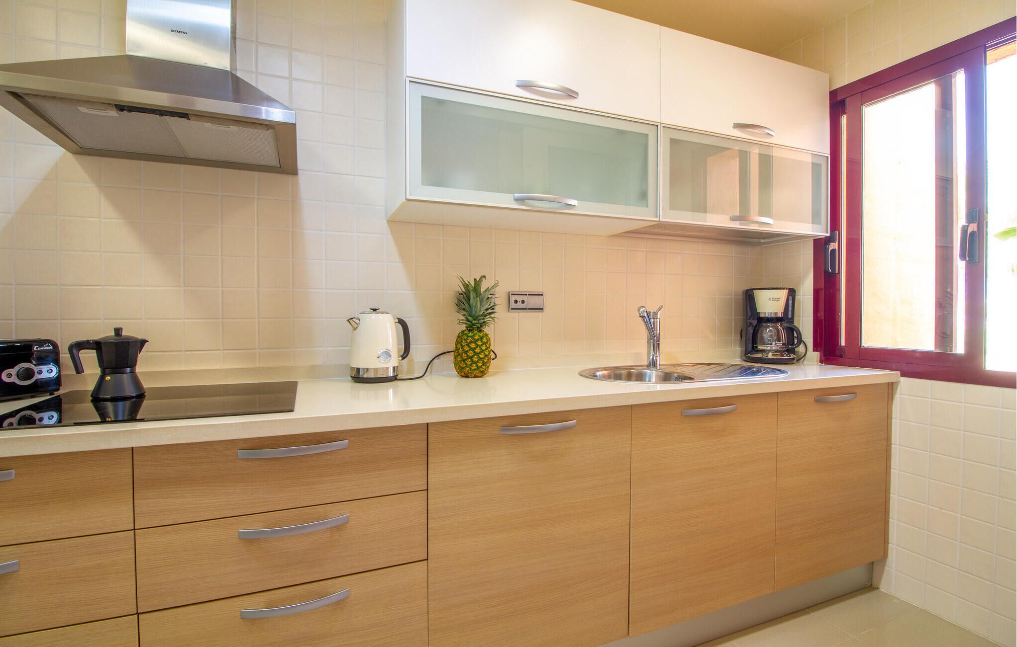 Una cocina con campana de acero inoxidable, cafetera, tetera y una piña sobre la encimera.