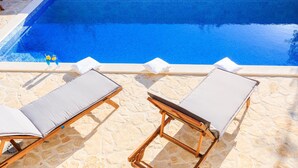 A poolside area with two wooden lounge chairs and a stone wall. - Gorgeous home in Kastel Sucurac (Kastel Sucurac)