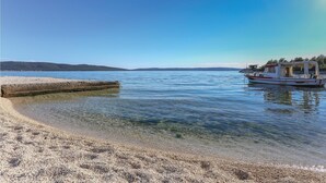 A clear beach with calm waters, a boat docked on the right, and a distant shoreline. - Gorgeous home in Kastel Sucurac (Kastel Sucurac)