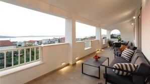 A balcony with a sofa and table, overlooking a body of water and buildings. - Gorgeous home in Kastel Sucurac (Kastel Sucurac)