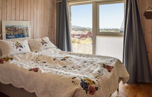 Relax in a serene bedroom with a large bed, wooden paneled walls, and a window offering a view of a nearby building and grassy field.