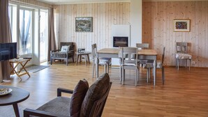 A living room with a TV, a fireplace, wooden walls, and a dining area.