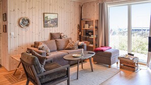 A cozy living room with a sofa, armchair, and ottoman, a coffee table, and a bookshelf.