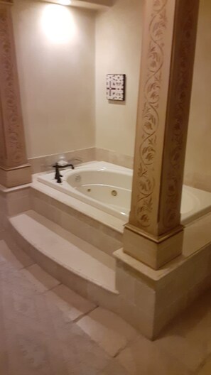 A bathroom with a bathtub, a shower, and a toilet. There is a decorative column with a floral pattern.