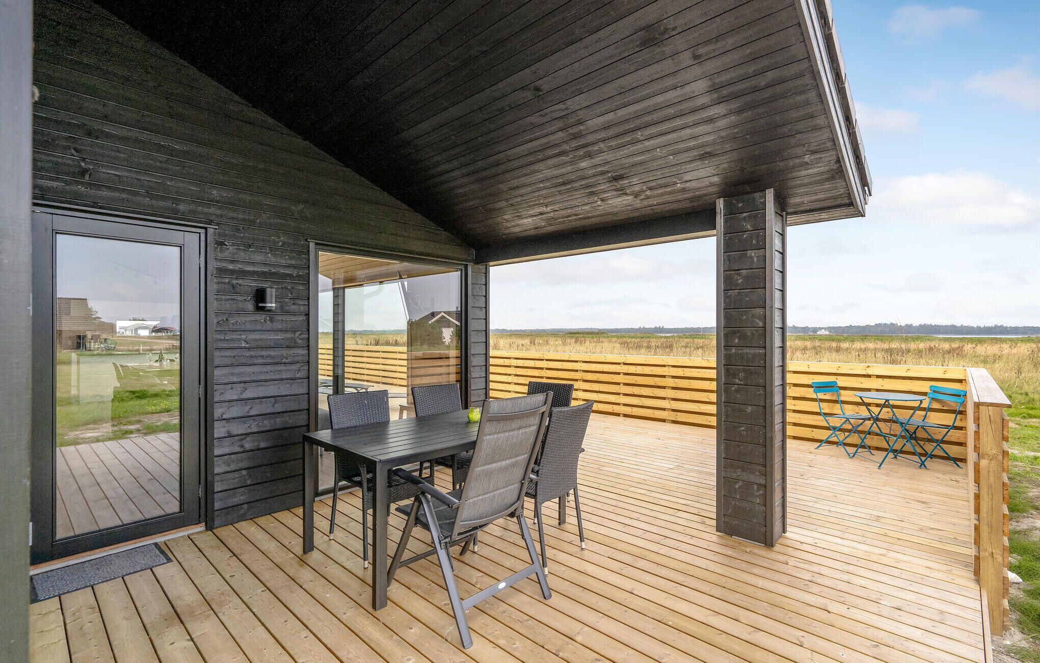 En träveranda med ett bord och stolar, och en glasdörr som leder ut till en utsikt över en gräsklädd äng.