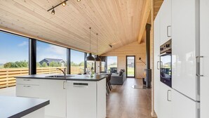 A modern kitchen with a large island, wooden ceiling, and large windows offering a view of the outdoors. - Stunning home in Storvorde with WiFi (Storvorde)
