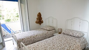 Due letti singoli con testiere abbinate e biancheria da letto fantasia in una stanza con una porta scorrevole in vetro che dà su uno spazio esterno.