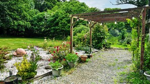 Ein Garten mit Holz-Pergola, Kiesweg und verschiedenen Pflanzkübeln.