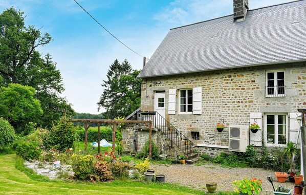 Une maison en pierre avec un jardin, un pont en bois et un chemin de gravier.