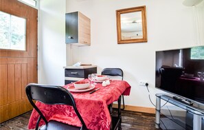 Un petit coin repas avec une table dressée pour deux personnes, un téléviseur et un meuble en bois placé au-dessus de la table.