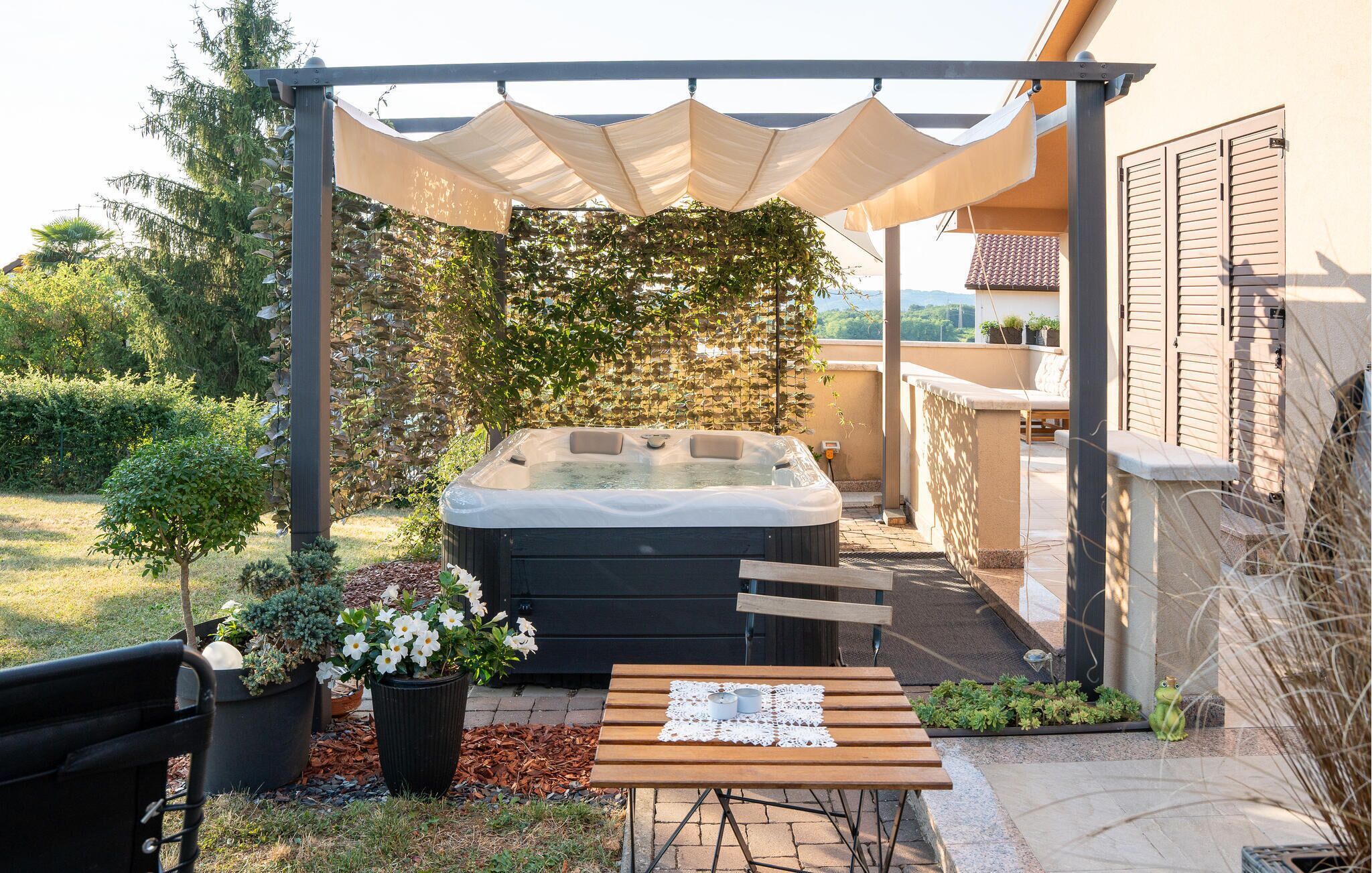 Un bain à remous installé sous une pergola, avec vue sur une maison et un jardin.