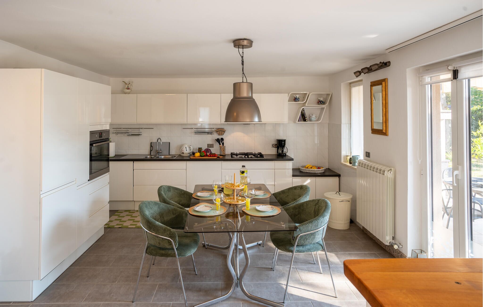 A modern kitchen with white cabinets, a dining table with chairs, and a hanging light fixture.
