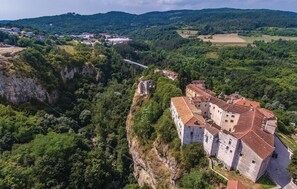 A historic stone building with a red-tiled roof, situated on a cliff overlooking a valley.