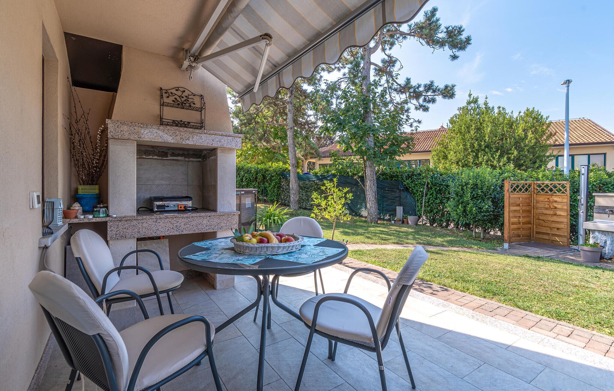 An outdoor patio with a grill, chairs, and a table with fruit.