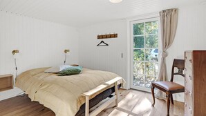 Een slaapkamer met een bed, een houten stoel, een raam met gordijnen en een kapstok aan de muur.