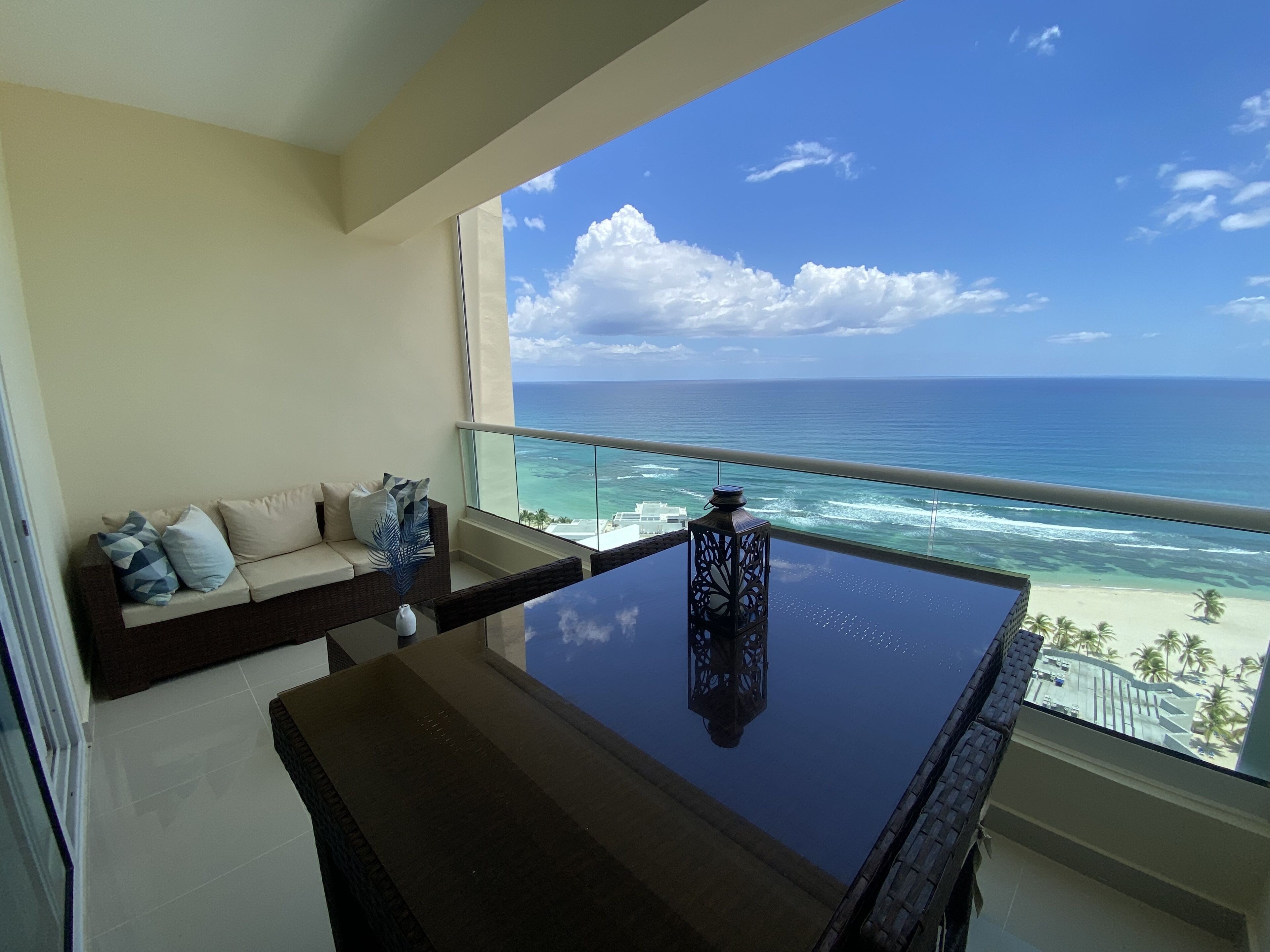 Een balkon met een glazen tafel en een bank, gericht op uitzicht over het strand.