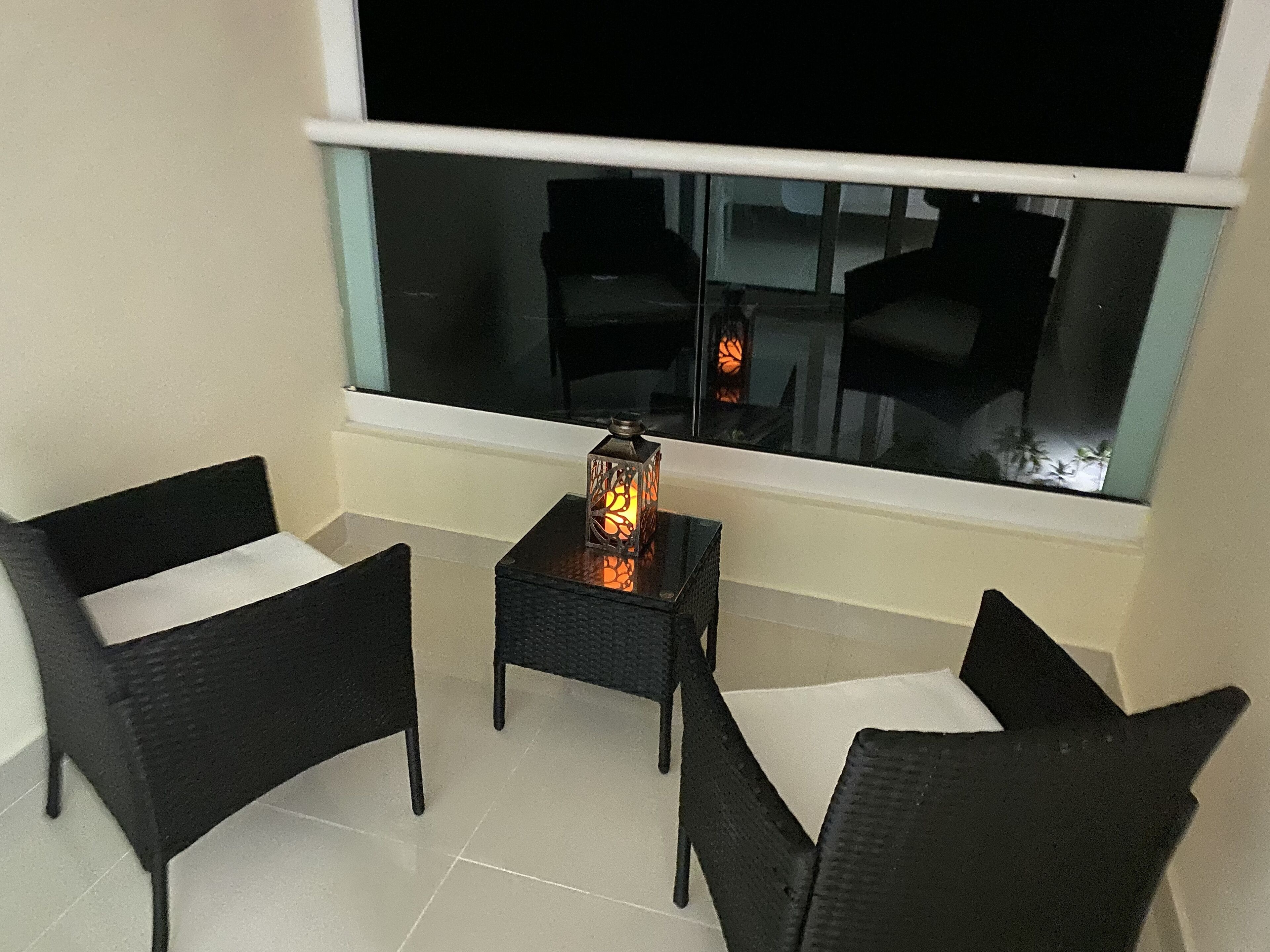 Un piccolo balcone con due sedie in vimini nero, un tavolino e una lanterna decorativa.