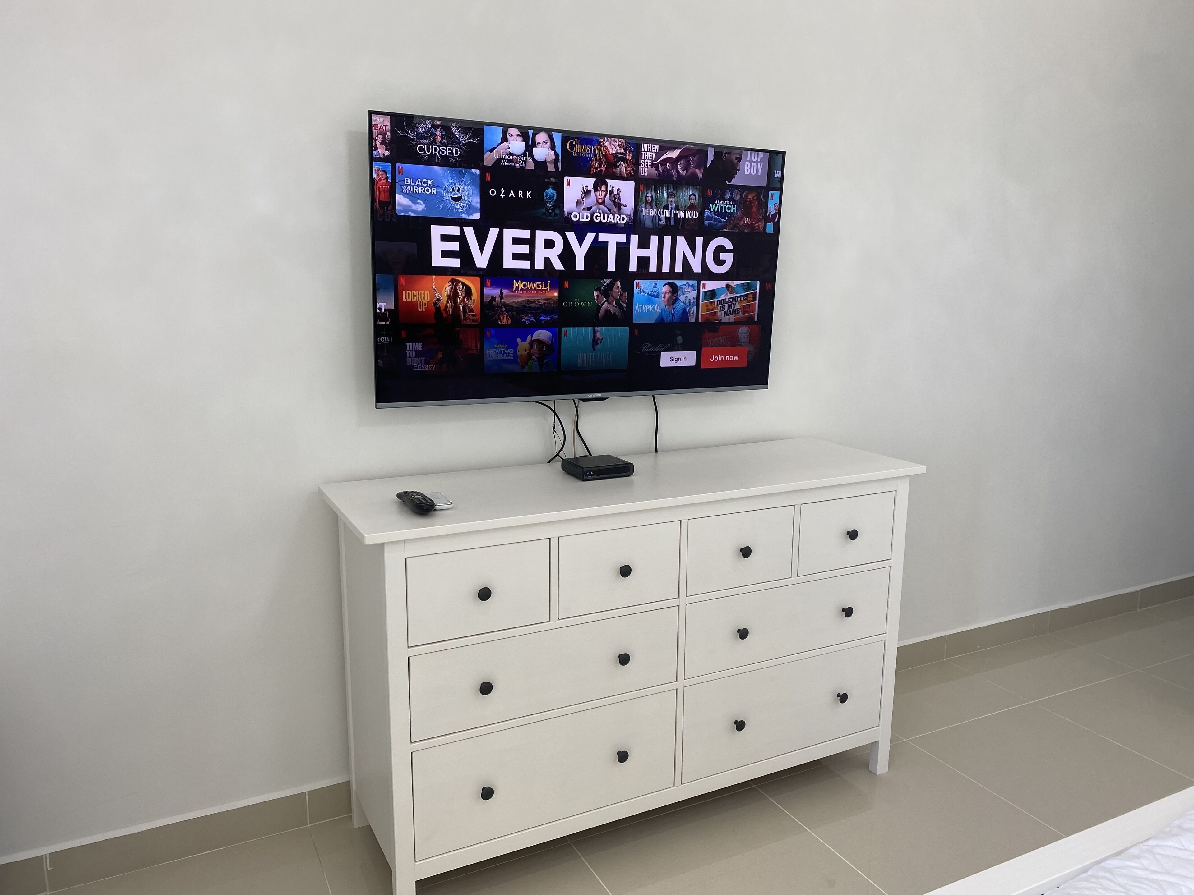 Seinälle asennettu litteänäyttöinen televisio, jossa näkyy useita suoratoistopalveluita. Television alla on valkoinen lipasto, jossa on useita laatikoita.
