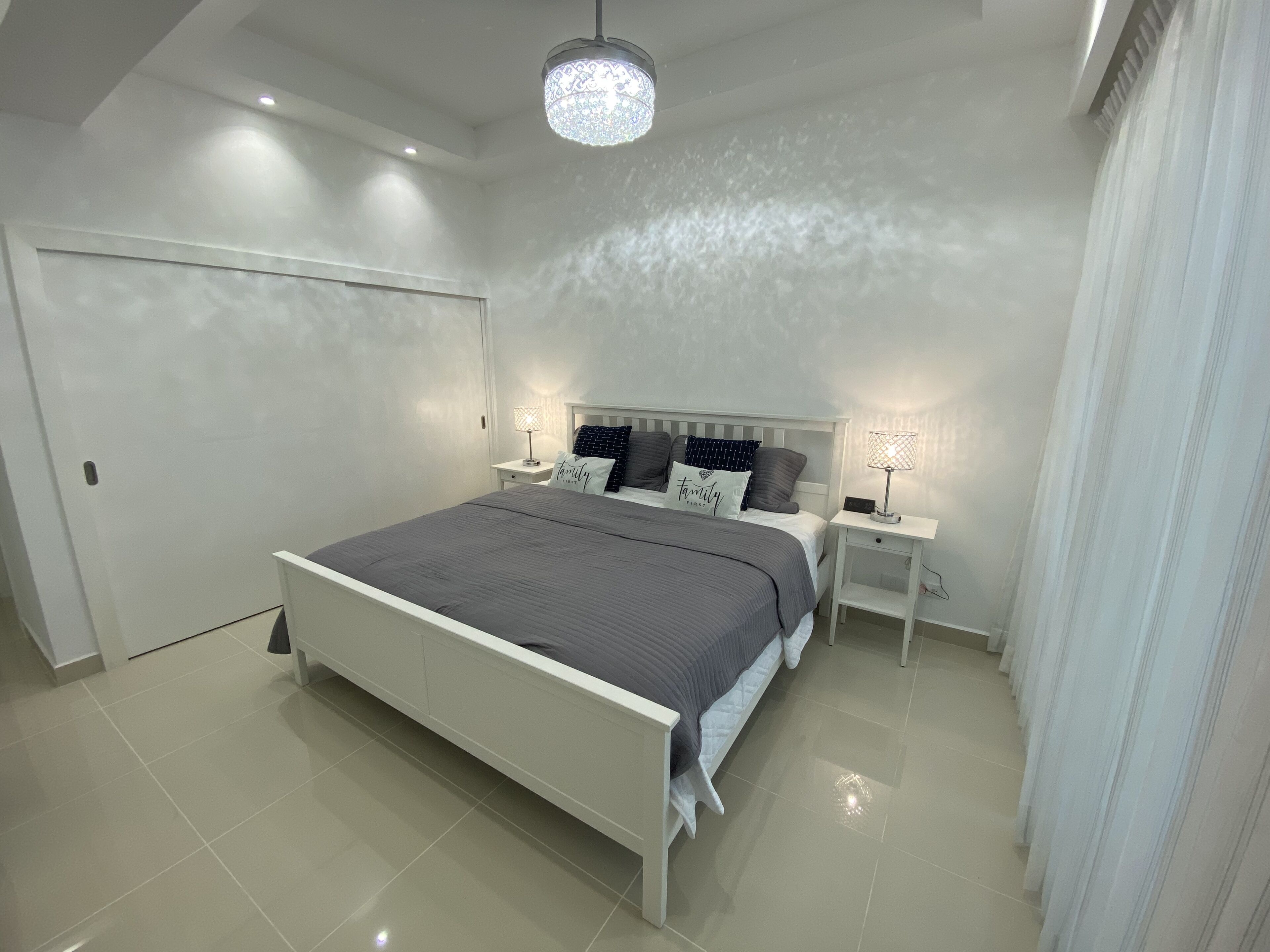 Une chambre à coucher moderne avec un grand lit, deux tables de chevet et un lustre.