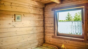 Une pièce de cabane en bois avec une fenêtre, un tableau encadré au mur et un banc en bois.