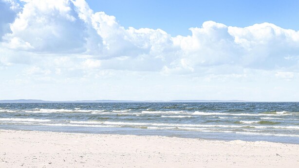 Une plage avec un ciel dégagé et des vagues sur l’océan.