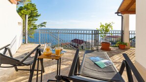 Un balcon avec vue sur la mer, une table avec des boissons et des fauteuils confortables.