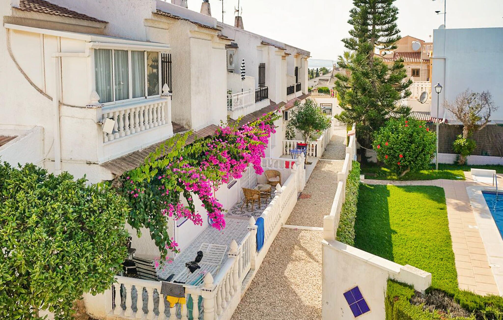 A residential area with white buildings, a garden, and a swimming pool.