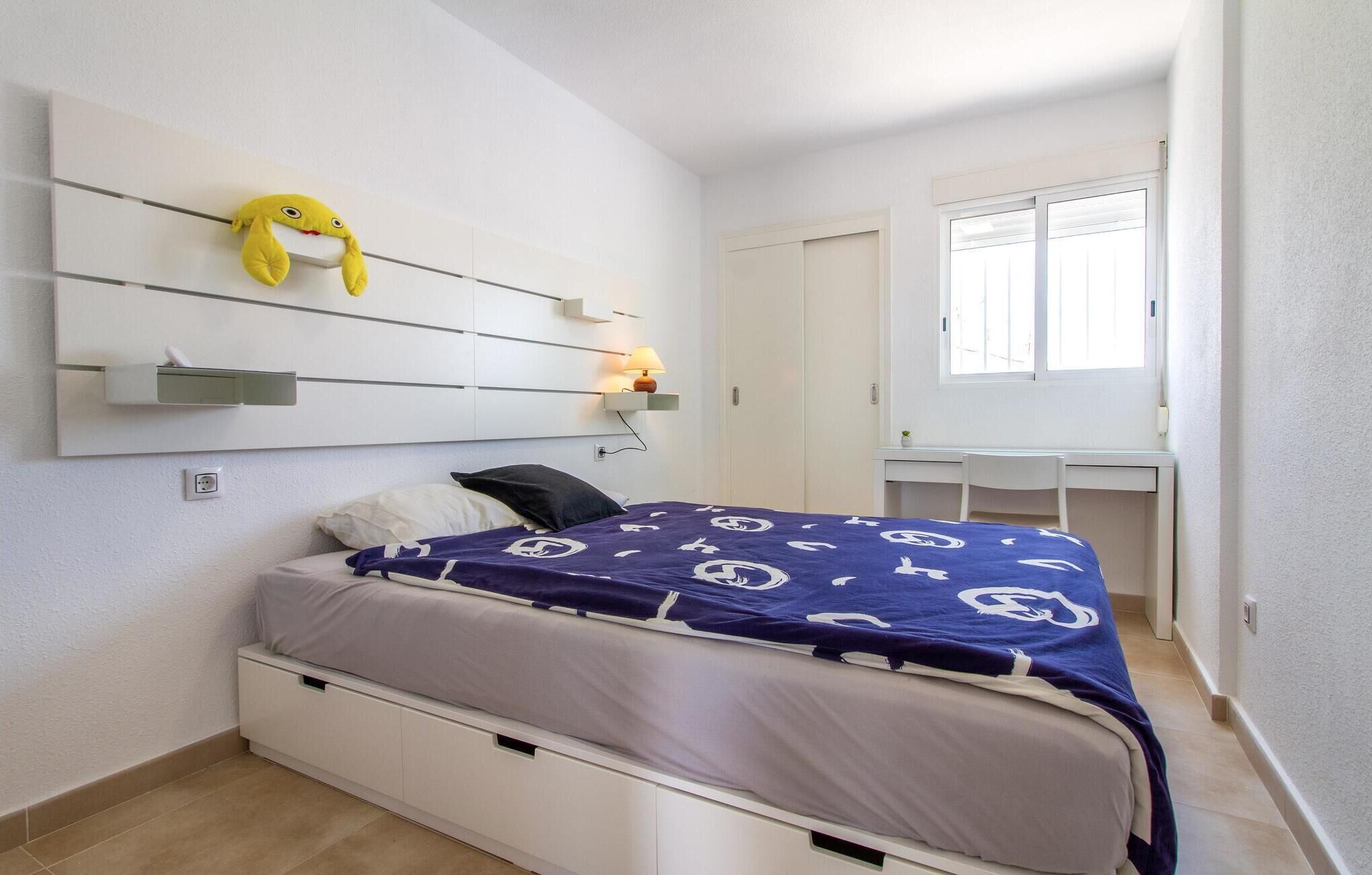 A bedroom with a bed, a desk, and a window.