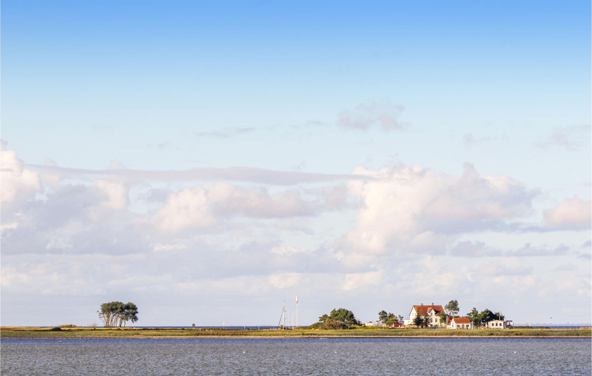 A coastal landscape with a house near the water, a lighthouse, and a clear sky.