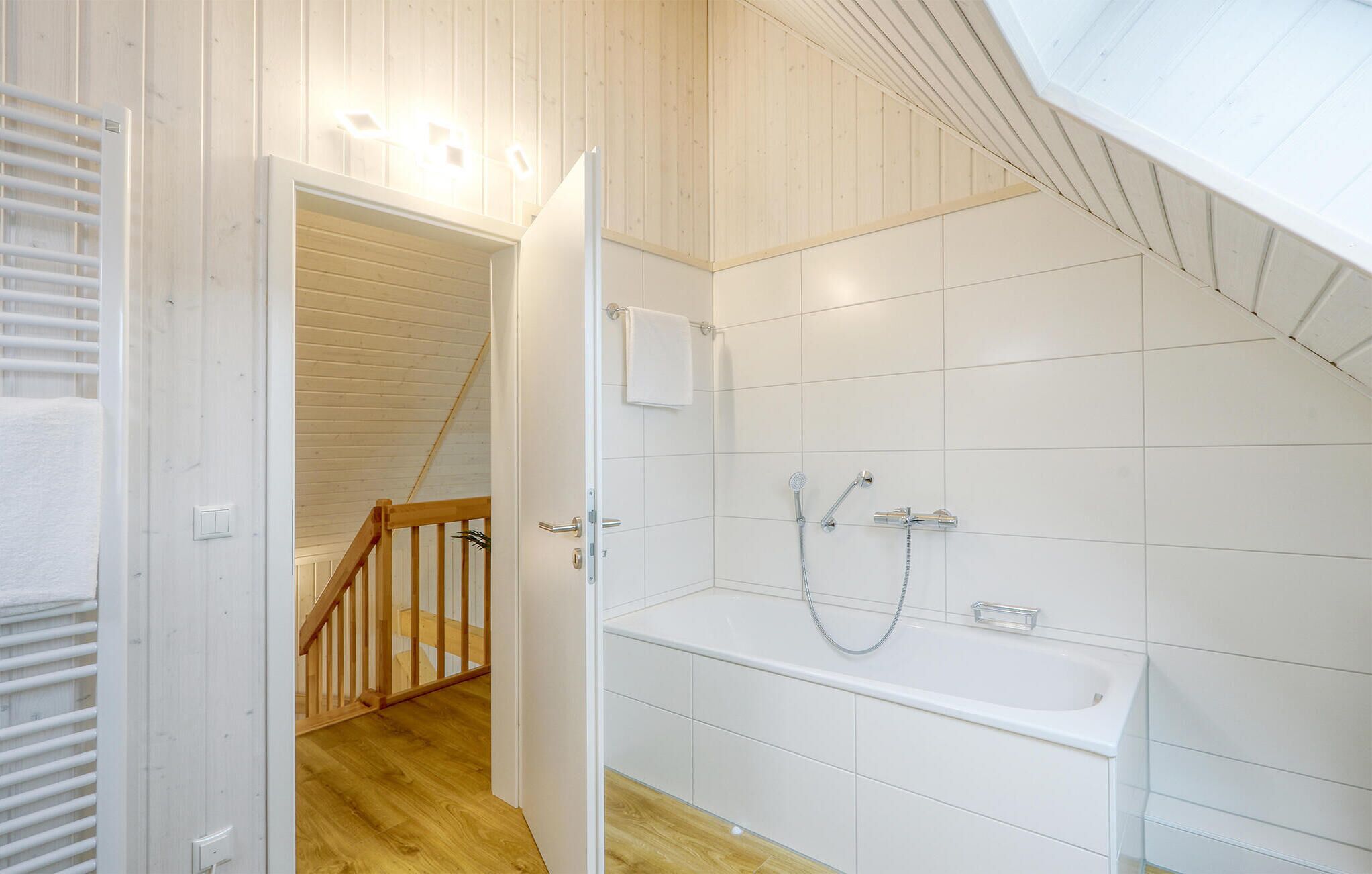 Un baño con bañera, ducha y una escalera de madera que sube a una zona en altura.