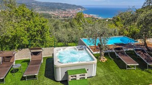 Ein Whirlpool, umgeben von Liegestühlen und einem Pool, mit Blick auf eine Küstenstadt und das Meer.