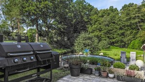 Een barbecue met een waterpartij en potplanten in een aangelegde tuin.