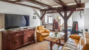 Een woonkamer met een televisie, leren fauteuils, een houten salontafel en een keuken op de achtergrond.