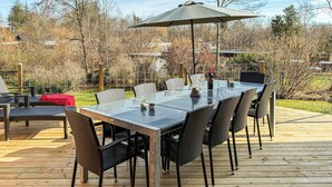 An outdoor dining area with a glass table and wicker chairs, surrounded by a wooden deck and a metal fence. - Pet friendly home in Farsø with sauna (Farsø)