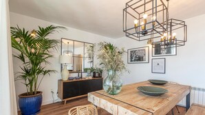 A dining area with a wooden table, a vase with dried plants, a blue pot with a plant, a wicker chair, a mirrored wall, and a modern light fixture. - Beautiful home in Nigüelas (Nigüelas)