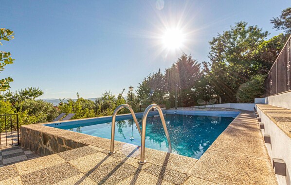 Une piscine rectangulaire, dotée de deux échelles en métal, entourée de carreaux de pierre et bordée d’un petit muret.