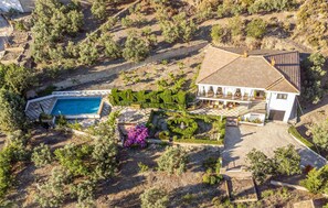 Vue aérienne d’une propriété comprenant une piscine, une grande maison avec un toit en tuiles et un jardin bien entretenu.