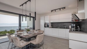 A modern kitchen with white cabinets, a black countertop, and a view of the sea. - 3 bedroom cozy apartment in Kostrena (Kostrena)